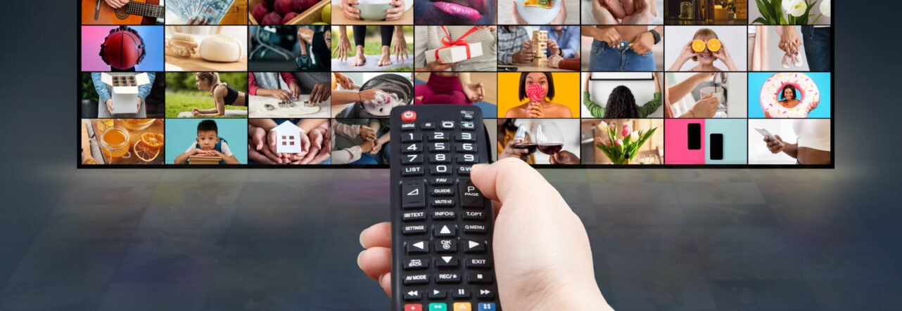 Hand Holding Remote Control Over Large Television Displaying Multiple Images